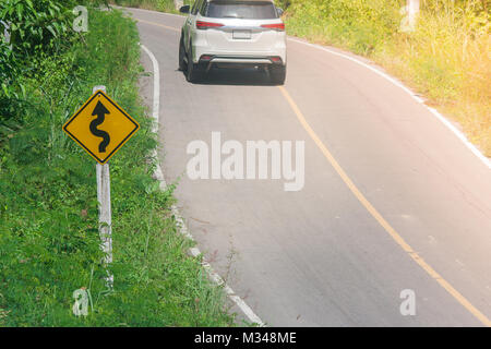 Traffico giallo segno 'Maze' di traffico sulla macchia verde di fianco alla strada con auto e la luce del sole sullo sfondo. Foto Stock