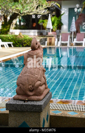 La scultura in pietra statua di un elefante seduto con il suo tronco fino felice e ridere da una piscina turchese in Thailandia in condizioni di luce diurna Foto Stock