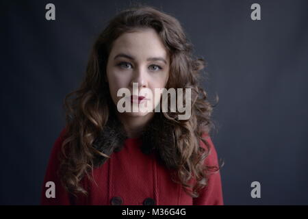 Dai capelli scuri in stile vintage ragazza in un rivestimento rosso con labbra rosse- isolate su un fondo di colore grigio scuro Foto Stock