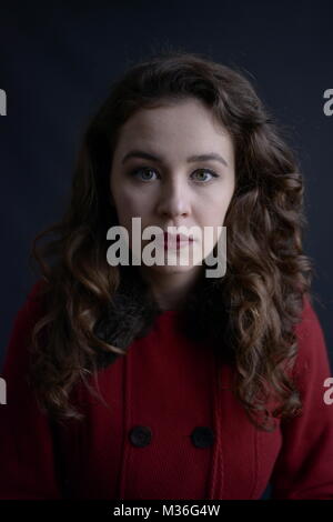 Dai capelli scuri in stile vintage ragazza in un rivestimento rosso con labbra rosse- isolate su un fondo di colore grigio scuro Foto Stock