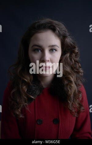 Dai capelli scuri in stile vintage ragazza in un rivestimento rosso con labbra rosse- isolate su un fondo di colore grigio scuro Foto Stock