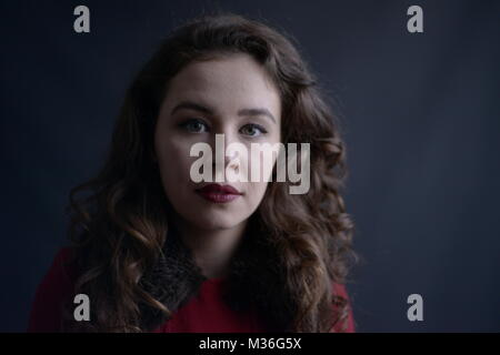 Dai capelli scuri in stile vintage ragazza in un rivestimento rosso con labbra rosse- isolate su un fondo di colore grigio scuro Foto Stock