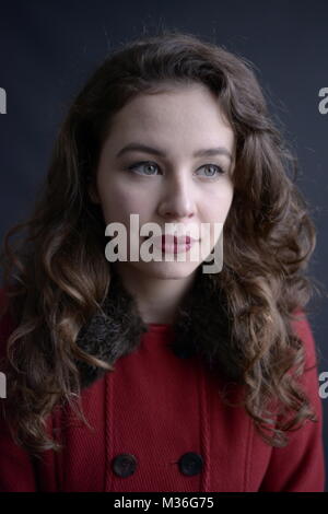 Dai capelli scuri in stile vintage ragazza in un rivestimento rosso con labbra rosse- isolate su un fondo di colore grigio scuro Foto Stock