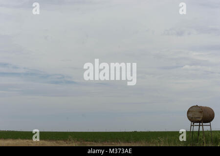 Vecchio arrugginito serbatoio acqua e canna sulle pianure sotto un aspetto lattiginoso cielo bianco Foto Stock