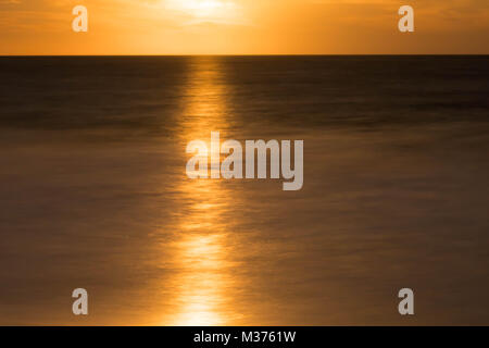 Full Moon Rising su una calma e scintillante oceano in un golden cielo notturno Foto Stock