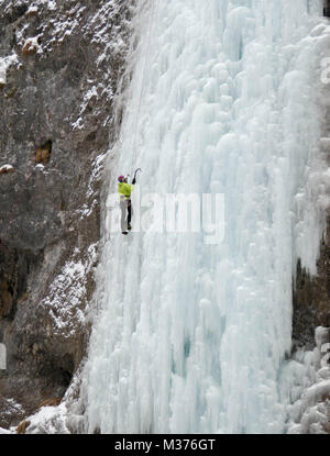 Maschio ice climber in una giacca gialla su una ripida cascata ghiacciata di arrampicata su ghiaccio a Sottoguda nelle Dolomiti Foto Stock