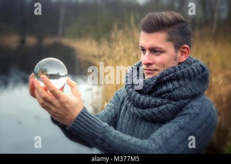 Bella bionda uomo di fronte lago in possesso di una sfera di vetro Foto Stock