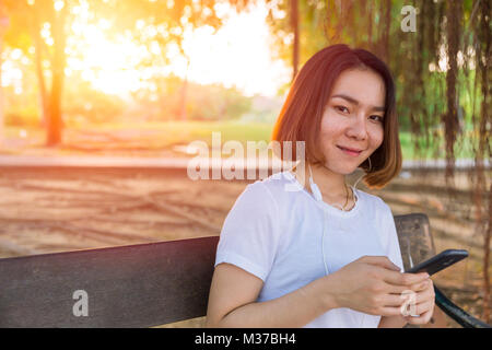 Asian Teen sorriso ascoltando la musica dal suo telefono nel parco per rilassarsi Foto Stock