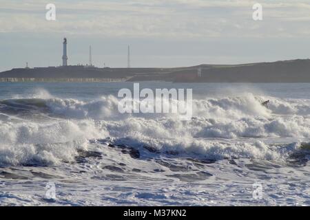 In Crash il Mare del Nord tempesta onde sulla spiaggia di Aberdeen, Girdleness faro in background. La Scozia, Regno Unito. Foto Stock