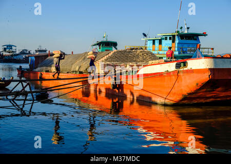 I lavoratori sono carico di sacchi di cemento su una barca in porto alla periferia della città sul fiume Irrawaddy Foto Stock