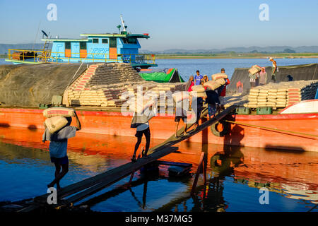 I lavoratori sono carico di sacchi di cemento su una barca in porto alla periferia della città sul fiume Irrawaddy Foto Stock