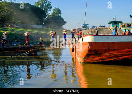 I lavoratori sono carico di sacchi di cemento su una barca in porto alla periferia della città sul fiume Irrawaddy Foto Stock