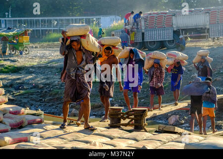 I lavoratori sono carico di sacchi di cemento su una barca in porto alla periferia della città sul fiume Irrawaddy Foto Stock