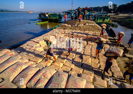 I lavoratori sono carico di sacchi di cemento su una barca in porto alla periferia della città sul fiume Irrawaddy Foto Stock