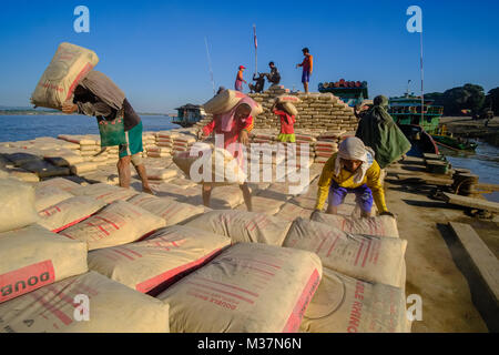 I lavoratori sono carico di sacchi di cemento su una barca in porto alla periferia della città sul fiume Irrawaddy Foto Stock