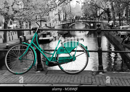 Una foto di un solitario azure bici sul ponte sul canale di Amsterdam. Lo sfondo è bianco e nero. Foto Stock
