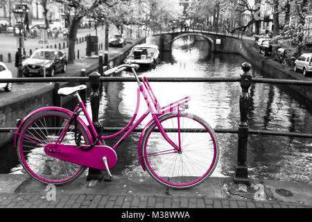 Una foto di una solitaria bicicletta rosa sul ponte sul canale di Amsterdam. Lo sfondo è bianco e nero. Foto Stock