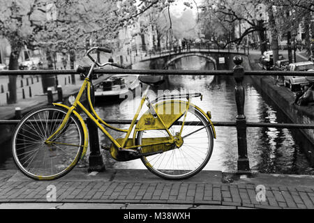 Una foto di una solitaria bici gialla sul ponte sul canale di Amsterdam. Lo sfondo è bianco e nero. Foto Stock