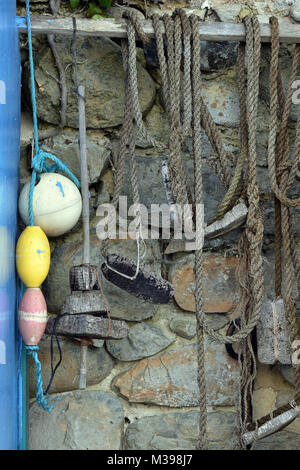 Una selezione di vecchie funi pesca blocchi appartamenti e affronta hanfing in un negozio di pescatori contro un muro di pietra. Rustica shabby chic e disegni costiere. Foto Stock