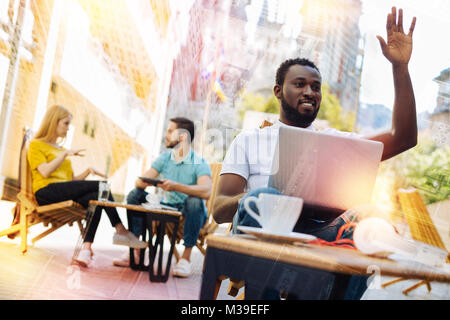 Bello studente alzando la mano e sorridere mentre chiamando un cameriere Foto Stock