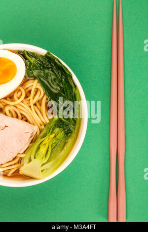Ciotola di stile Giapponese la carne di maiale Ramen noodle soup con pak choi e un uovo sodo contro uno sfondo verde Foto Stock