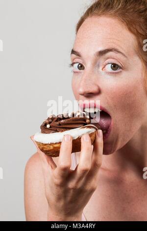 Modello rilasciato. Close-up di donna mangiando cioccolato ciambella. Foto Stock