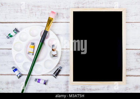 L'acquerello tavolozza e un pennello bianco su sfondo di legno con blackboard e spazio copia .Template mock up per aggiungere il tuo design e copiare sp Foto Stock