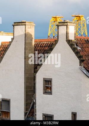 Leith, Edimburgo, Scozia, Regno Unito. Incongrua giustapposizione di enorme giallo sole turbina eolica piattaforme, chiamato giacche per centrali eoliche, in Leith Harbour che torreggiano sulla pantile tetto di uno degli edifici più antichi di Leith, xvii secolo agnello della casa di un ex Hanseatic Leith Merchant House, ora casa per l'architetto che ha ripristinato, Nicholas Groves Raines. Queste piattaforme di arrivare in Leith sul loro modo Nord per fornire una struttura secondaria per le turbine in un offshore wind farm in Moray Firth Foto Stock