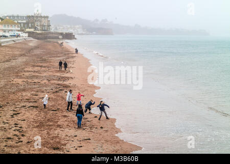 Famiglia godendo di febbraio half term holidays nonostante la pioggia, la scrematura di pietre sulla spiaggia. Rainy inizia a metà termine rottura a Paignton, Torbay, Devon, Regno Unito. Credito: JHNews / Alamy Live News Foto Stock