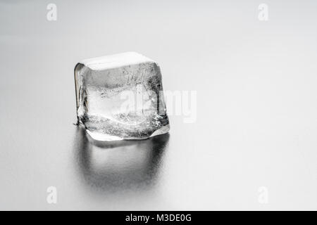 Close up di un quadrato singolo cubo di ghiaccio su una pianura leggermente la superficie riflettente Foto Stock