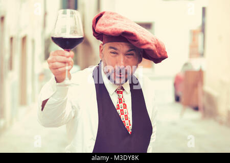 Coppia eccentrico uomo che offre un bicchiere di self made vino guardando eccitato a telecamera. Foto Stock