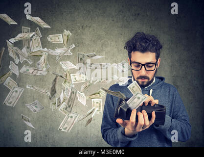 Uomo triste guardando al suo portafoglio con denaro dollaro banconote volare al di fuori Foto Stock