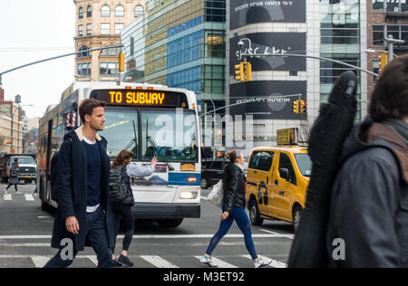 Pedoni che attraversano nel traffico di fronte ad un pubblico di autobus che porta alla stazione della metropolitana di New York City Foto Stock