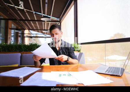 Lavoratore di ufficio ordinamento di carte sul tavolo vicino al computer portatile. Foto Stock