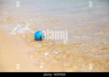 Mini globo sulla spiaggia lavata da onde Foto Stock