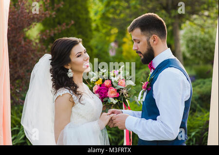 Ritratto di felice coppia anelli di scambio durante la loro cerimonia di matrimonio all'aperto Foto Stock