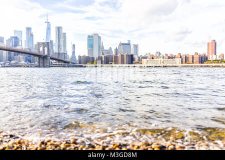 Rocky spiaggia ghiaiosa shore acqua in East River con vista di NYC New York City cityscape skyline e bridge, nessuno in Brooklyn Foto Stock