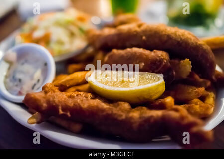 Macro closeup profondo di pesce fritto e patatine martoriata marrone di filetti di crosta dorata nel ristorante con fettina di limone, salsa tartara, il lato piatto sul tavolo in anche Foto Stock