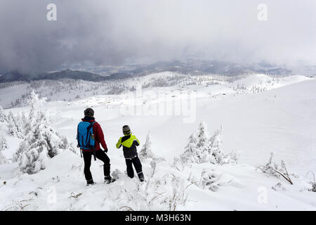 La madre e il figlio in piedi sulla parte superiore di una coperta di neve montagna guardando giù per la valle, Velika planina, Slovenia. Foto Stock