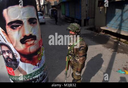 Srinagar, India. Xi Febbraio, 2018. Un soldato di paramilitari sta di guardia accanto a un poster con il ritratto del Maqbool Bhat durante lo spegnimento a Srinagar, India Kashmir amministrato. Coprifuoco-simili restrizioni sono state imposte in parti di Srinagar città al seguito di una chiamata per sciopero dei gruppi separatisti per commemorare l anniversario della morte di Maqbool Bhat, il Jammu e Kashmir Liberation Front (JKLF) fondatore che fu impiccato in Delhi 34 anni fa.In altre parti della vallata, un arresto completo del sistema viene osservata. Negozi, stabilimenti commerciali sono chiusi e molto pochi veicoli vengono visti da r Foto Stock