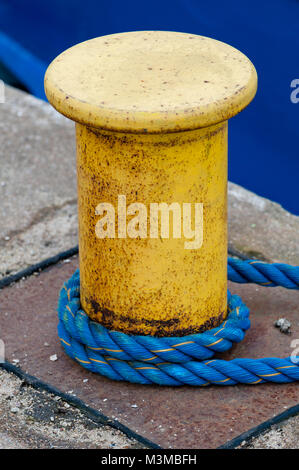 Rusty bollard giallo con blu linea moorig alla luce del giorno. Foto Stock