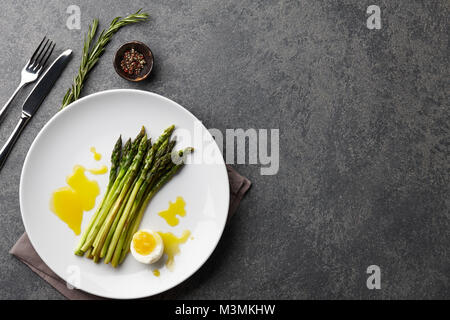 Asparagi al forno con uova sode o in grande piastra bianca su sfondo di pietra, vista dall'alto Foto Stock