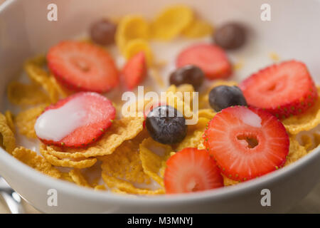 Corn flakes con frutti di bosco in bianco ciotola per la prima colazione sul tavolo Foto Stock