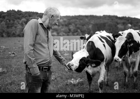 Foto in bianco e nero di Senior agricoltore orgogliosamente guardare le proprie vacche in campagna all'esterno. Foto Stock