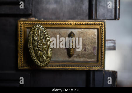 Vista frontale dettaglio closeup di vecchi vintage golden maniglia serratura della porta con intarsio metallico nero su sfondo di legno Foto Stock