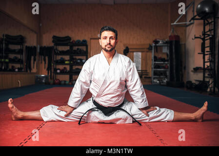 Arti marziali karate master in kimono bianco e nero della cinghia facendo stretching esercizio in palestra Foto Stock