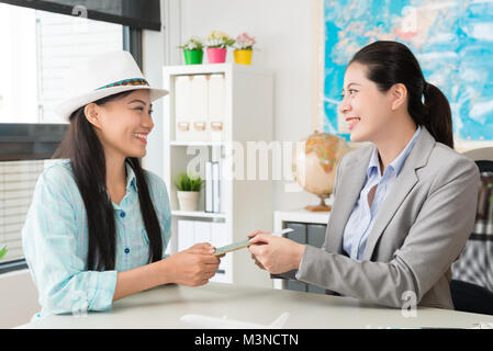 Professional giovane agente di viaggio azienda lavoratore di ufficio donna dando passaporto con biglietto aereo per il suo cliente viaggiatore. Foto Stock