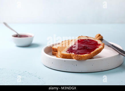 Toast con burro di arachidi e marmellata in un piatto di portata in ceramica bianca su sfondo blu sullo sfondo di calcestruzzo Foto Stock