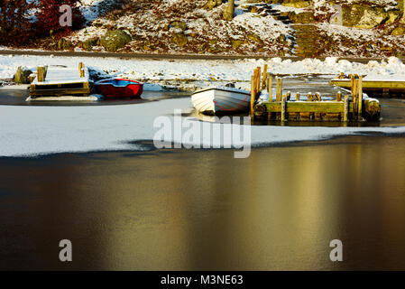 Due piccole imbarcazioni ormeggiate al molo e congelati bloccato dal freddo inverno. Bella riflessioni dei pontili in legno e il paesaggio nel ghiaccio. Foto Stock