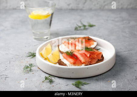 Aprire il panino con il salmone, la crema di formaggio e pane di segale in una piastra bianca su un cemento grigio sfondo Foto Stock